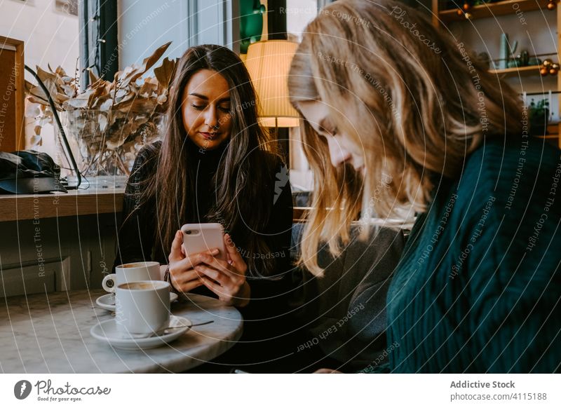 Female friends resting in cozy cafe women together coffee smartphone using joke casual weekend young meeting restaurant drink cup beverage coffee shop cheerful