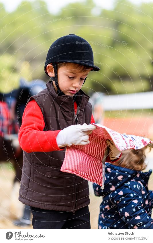 Little jockey with saddle pad boy equestrian school lesson carry prepare hobby kid child helmet safety horseback soft blanket sport training education childhood