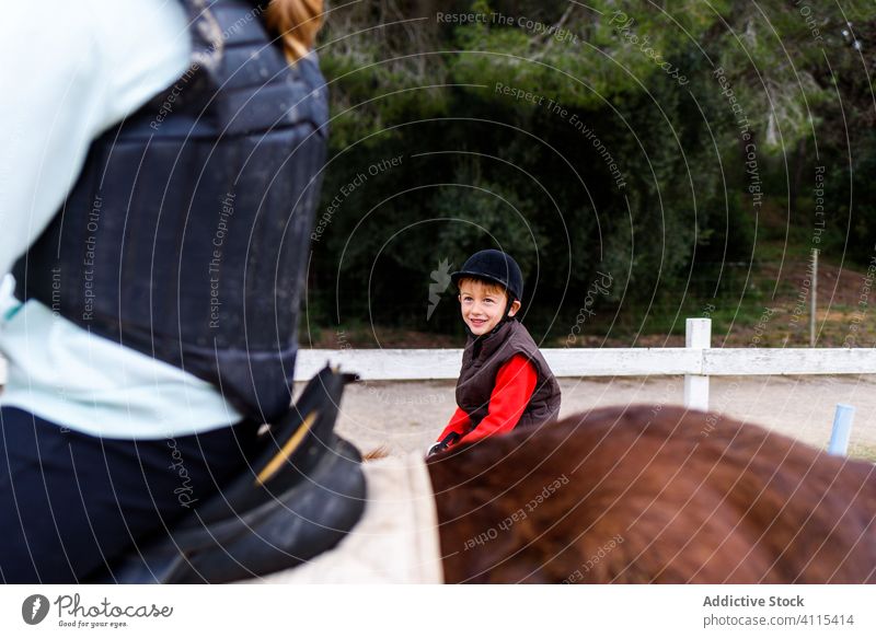 Kid and anonymous teenager during horseback riding lesson jockey ride school dressage arena boy girl pony equestrian kid child brown roan together saddle animal