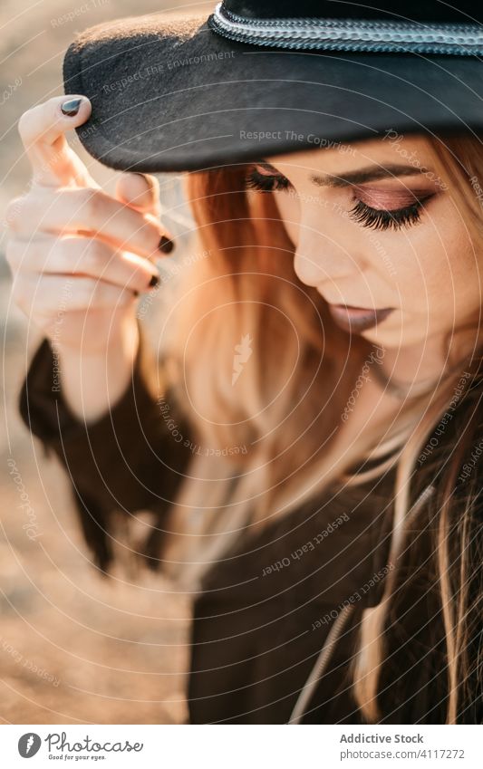 Trendy lady touching hat and looking down woman style makeup dark appearance manicure fashion serious female model glamour accessory trendy vogue cosmetic