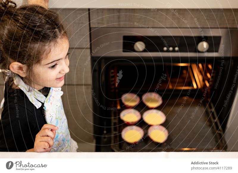 Cute girl preparing cupcakes at home cook oven kitchen smile ethnic bake weekend kid child modern apron dessert happy pastry raw food cheerful snack prepare