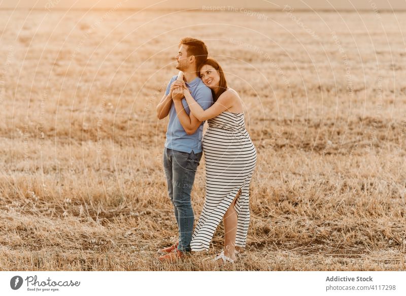 Couple awaiting baby hugging in field couple pregnant hay field sunset love touch belly together tender countryside man woman nature expect relationship