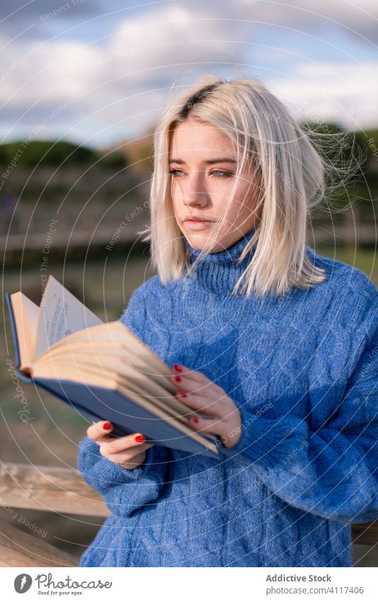 Pensive woman enjoying book in countryside read nature sweater young female casual blonde rest literature hobby happy charming style blue warm holiday travel