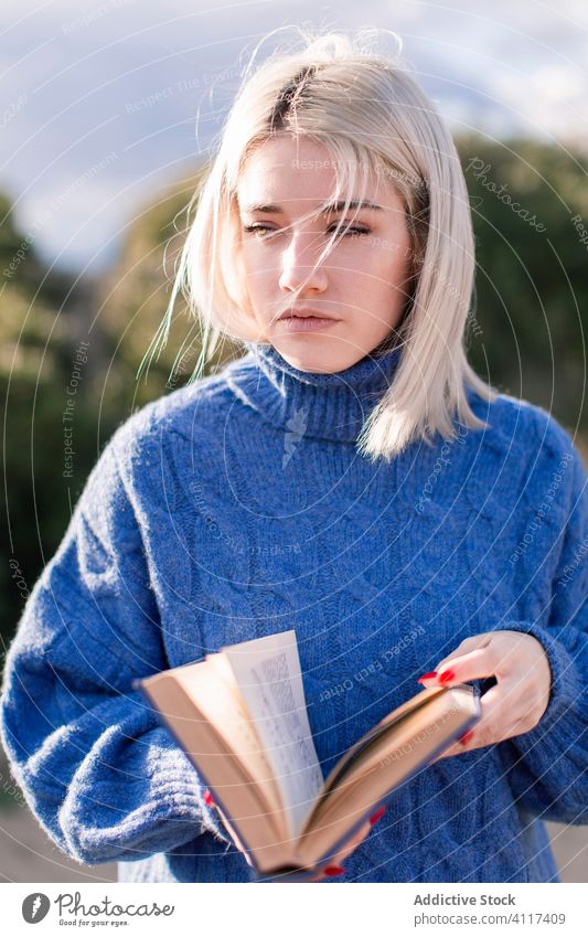 Pensive woman enjoying book in countryside read nature sweater young female casual blonde rest literature hobby happy charming style blue warm holiday travel