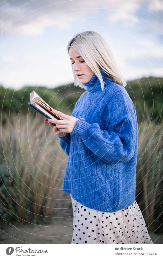 Young woman standing reading book blue sweater young casual serious nature blonde confident modern female education hobby student rest smart learn knowledge