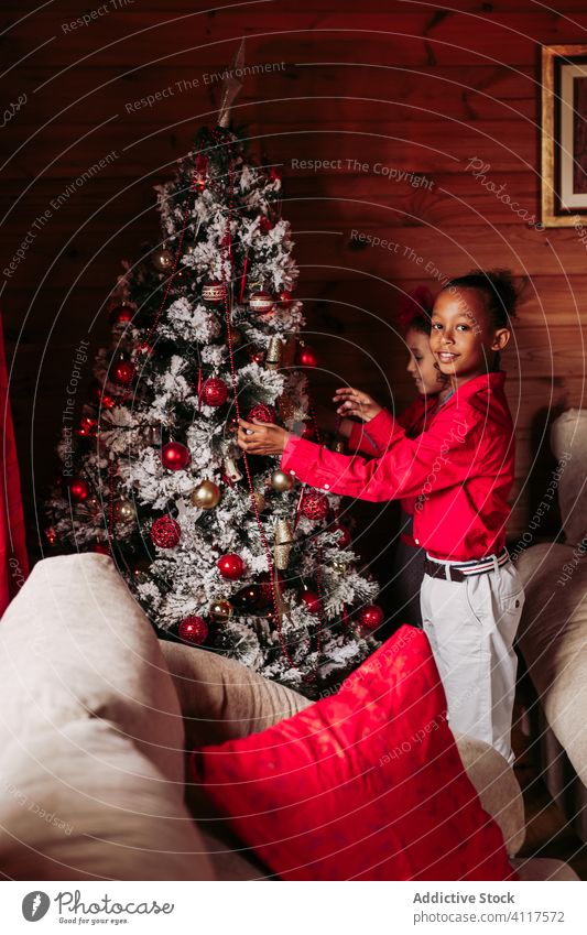 Happy kids decorating Christmas tree at home christmas decorate tradition rustic ethnic festive casual sibling together sister black african american red wooden