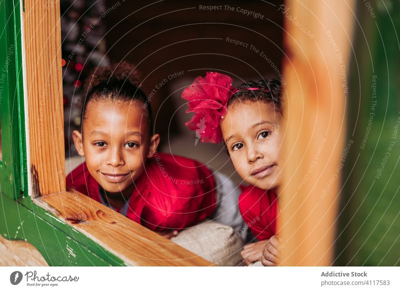 Cheerful ethnic children looking out window kid house happy sibling together cheerful wooden rural smile home lifestyle countryside joy little casual sister