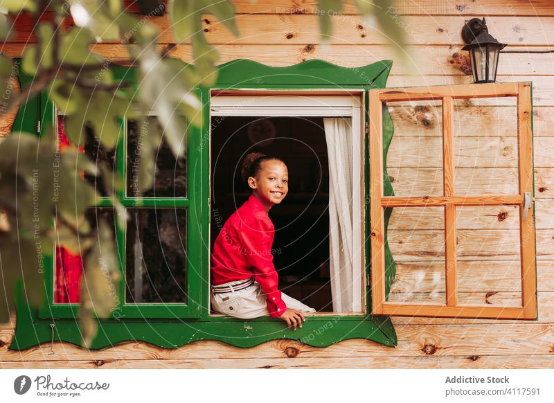 Happy ethnic kid looking out window house happy cheerful wooden rural smile home child lifestyle countryside joy little casual childhood black african american