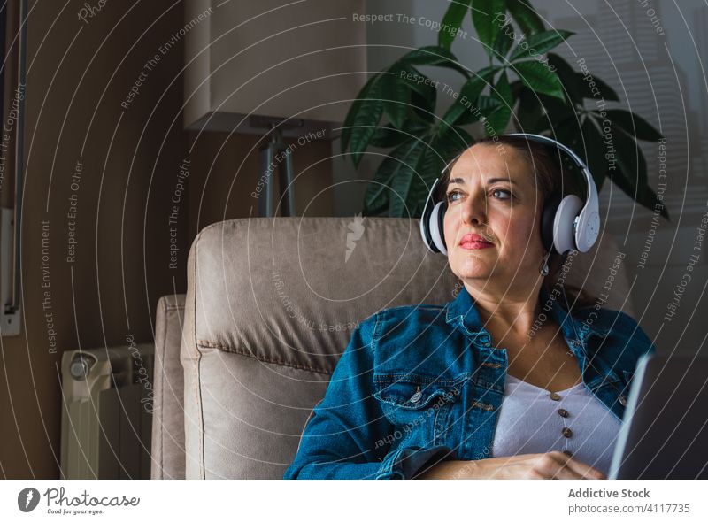 Adult freelancer with laptop woman music listen headphones using home female adult mature window armchair sit device gadget wireless modern internet job lady