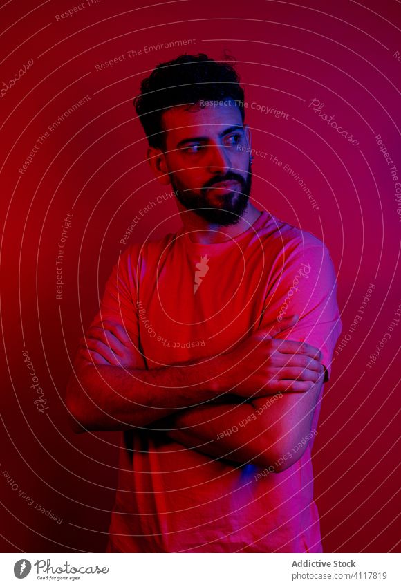 Confident bearded man under red light modern style serious confident arms crossed bright outfit male trendy t shirt apparel garment illuminate neon nightlife