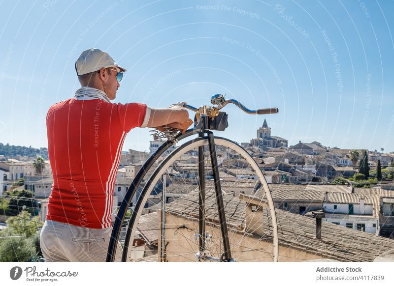 Male tourist with retro high wheel bicycle on viewpoint against scenery with old town man aged tourism sightseeing street travel ancient enjoy penny farthing