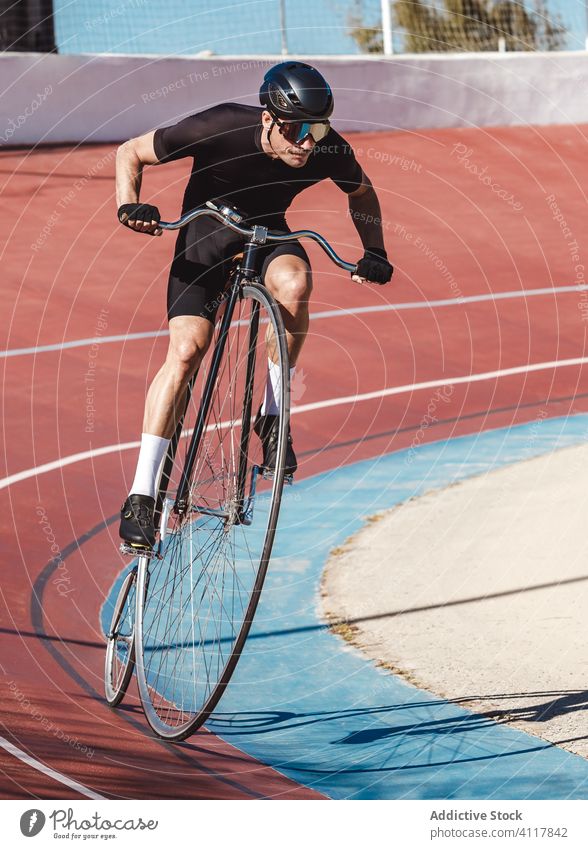 Determined sportsman riding high wheel bike while training alone at sports stadium bicycle ride cyclist athlete penny farthing active vehicle fit rider practice