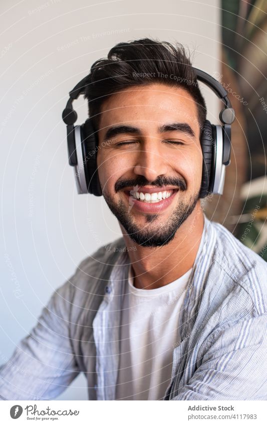 Bearded man listening to music with closed eyes smile home headphones ethnic happy rest weekend male headset cheerful sound beard fun cozy audio cool device