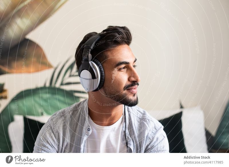 Bearded man listening to music and looking away smile home headphones ethnic happy rest weekend male headset cheerful sound beard fun cozy audio cool device