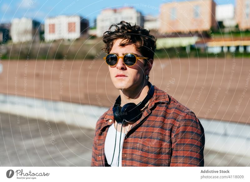 Stylish guy on city street man style urban hipster young outfit confident modern male sunglasses checkered shirt headphones casual trendy lifestyle town cool