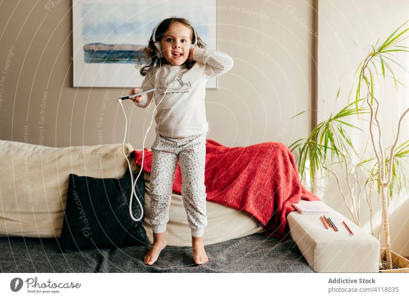 Cute little girl jumping on the couch and listening music with headphones cute posing home indoors window kid child portrait childhood colorful beauty children
