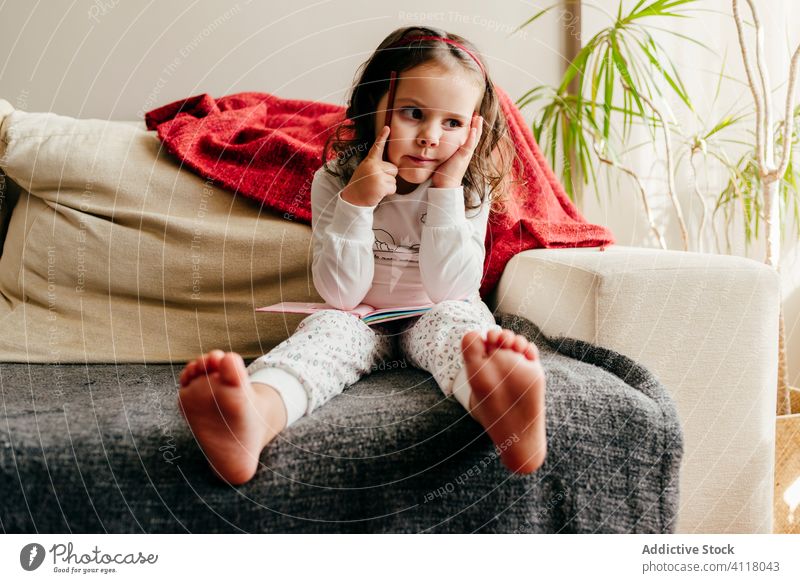 Cute little girl sitting on the couch with a notebook looking for inspiration cute posing home indoors window kid child portrait childhood colorful beauty