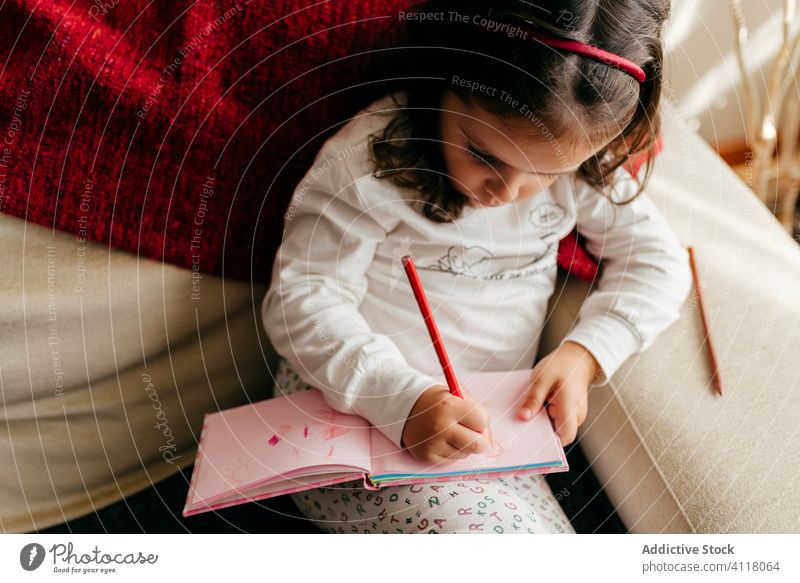 Cute little girl sitting on the couch and drawing in the notebook cute posing home indoors window kid child portrait childhood colorful beauty children daughter