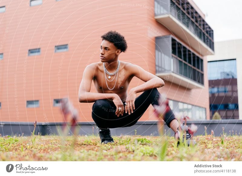 Ethnic male shirtless model with neck chains sitting on street man trendy necklace cool independent street style young confident modern black african american