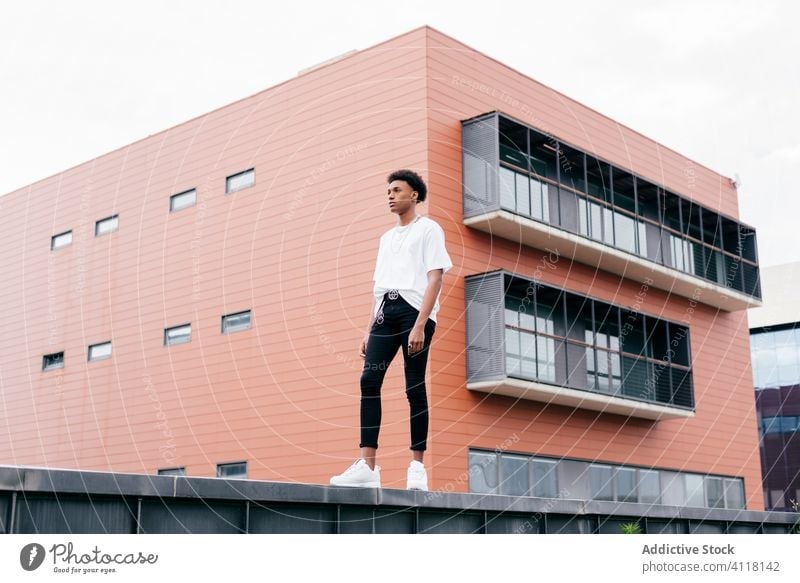 Fashionable ethnic man standing against modern building street style fashion trendy cool urban young city confident african american black contemporary outfit