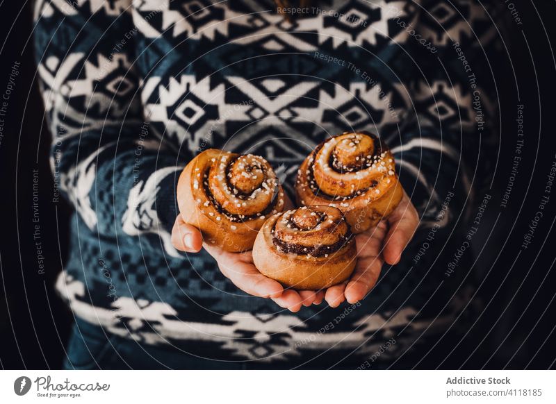 Crop person holding fresh cinnamon buns in hands roll bake delicious cozy sweater handful pastry warm dessert home holiday homemade tradition aromatic tasty