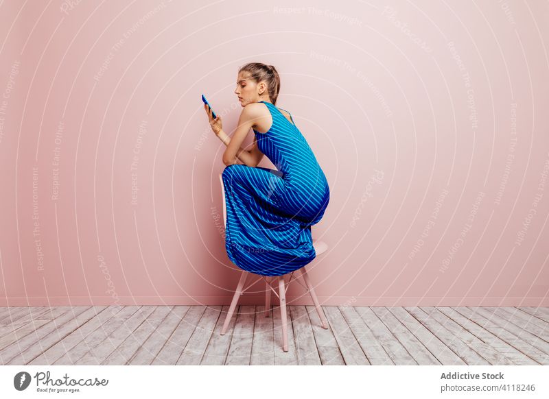 Woman on top of a chair using smartphone on pink background woman crouched stylish talk slim model female attractive fashion glamour natural cute gadget elegant