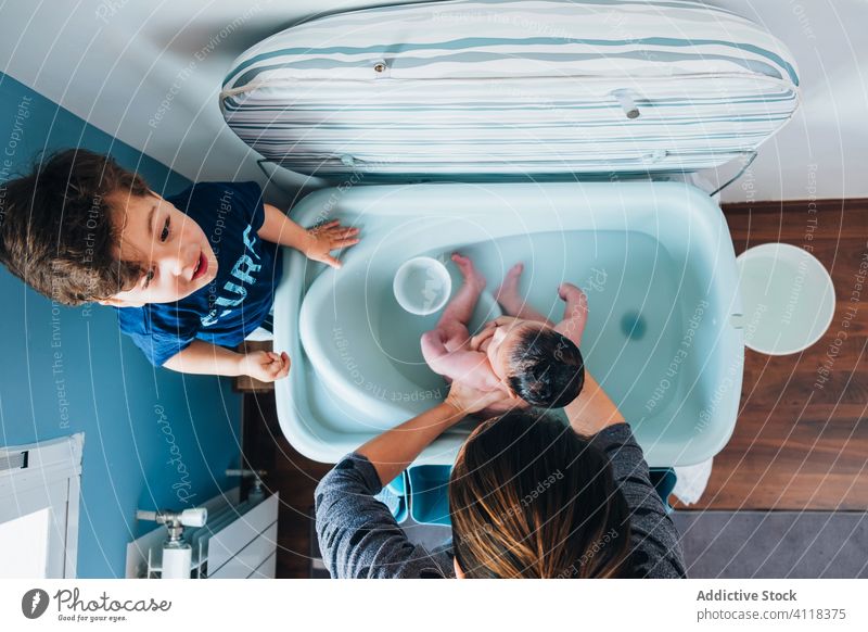 Mother with little son washing baby in bathtub woman mother children dibling care newborn bathroom ethnic bowl love gentle together cute help warm parent foam