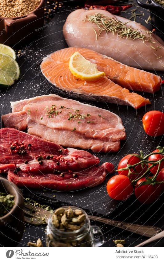Flat lay of proteins surrounded by spices and seasonings on table product meat salmon condiment fish fillet food pepper cutting board spoon aromatic assorted