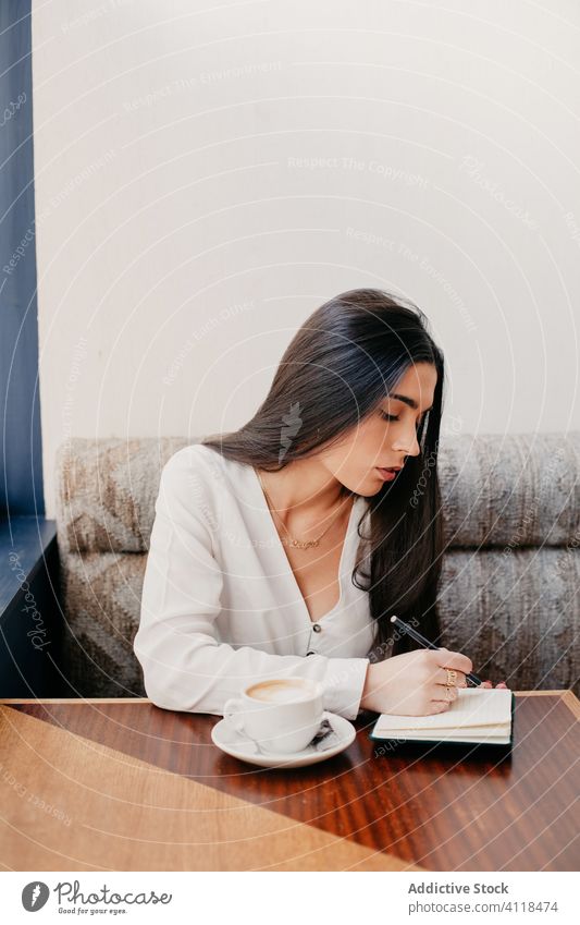 Woman writing in a notebook sitting in a bar female businesswoman cafe table lifestyle work girl restaurant caucasian brunette people person modern lady young