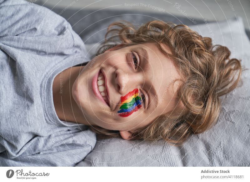 Happy boy with rainbow on face looking at camera home quarantine point at camera concept symbol smile lying floor blanket pillow kid child pandemic epidemic