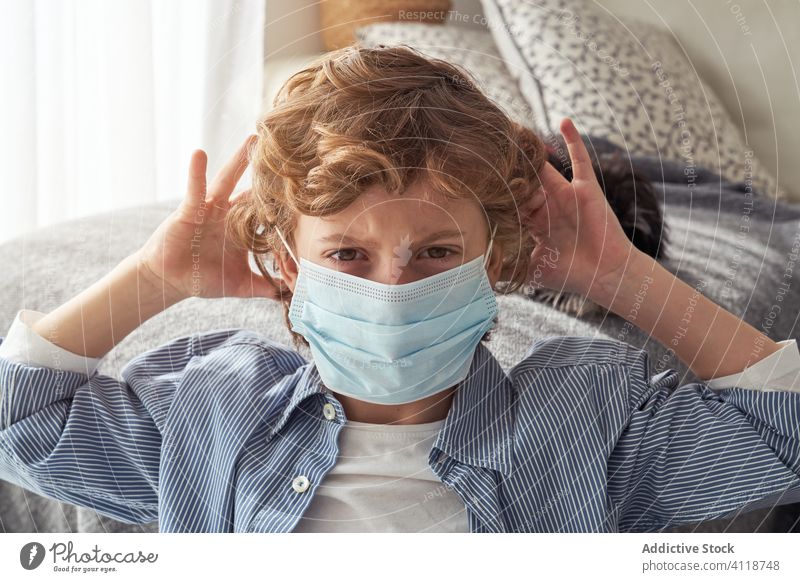 Displeased boy in medical mask at home quarantine displease frown hands behind head sofa pet treat care protect prevent coronavirus epidemic covid 19 pandemic