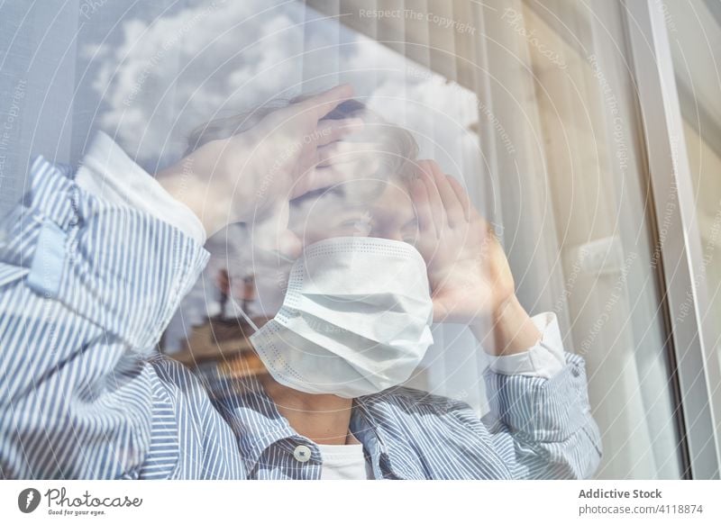 Boy behind window during quarantine boy mask medical home frown pandemic coronavirus covid 19 child kid childhood sad unhappy hygiene health care infection