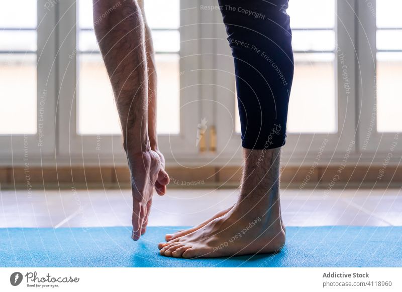 Focused male athlete stretching body in standing position on mat in light modern gym leg forward bend sport barefoot man arm flexible training focus effort
