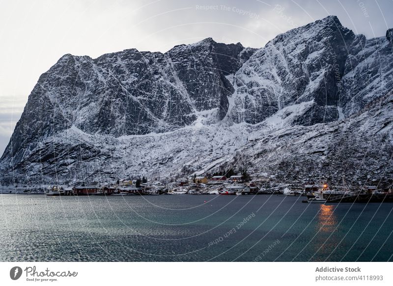 Picturesque scenery with coastal town at foot of snowy rocks under gray cloudy sky harbor mountain nature water highland ridge tourism range lofoten overcast