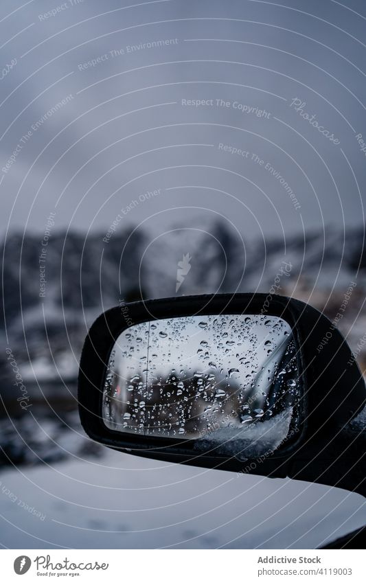 Car mirror covered with water drops against snowy terrain in overcast weather car winter reflection road trip wet norway auto travel highland tourism automobile