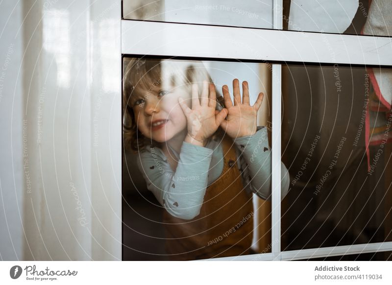 Happy little girl behind window happy home smile casual cute touch glass kid child cheerful childhood room playful curious rest lifestyle relax innocent cozy