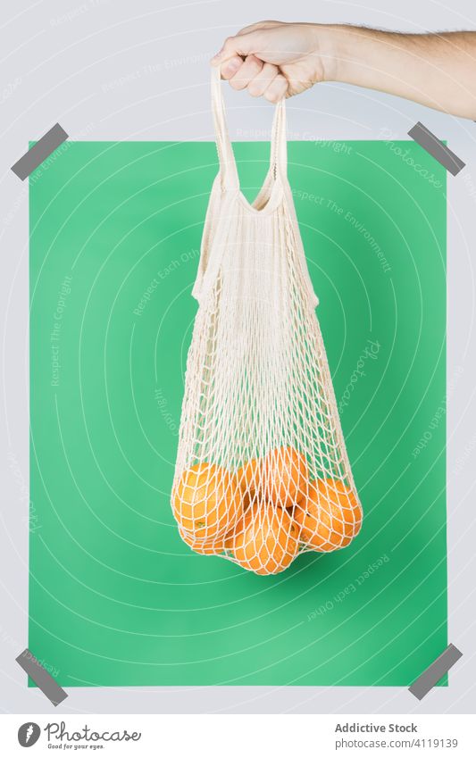 Crop person carrying string bag with oranges zero waste grocery concept eco friendly rectangle bright colorful organic shop green package net vivid sack vegan