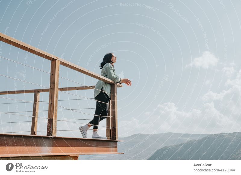 Woman in a balcony over a massive river and the mountains living the moment liberty and freedom concept, wellness during a sunny day white copy-space 20s 30s