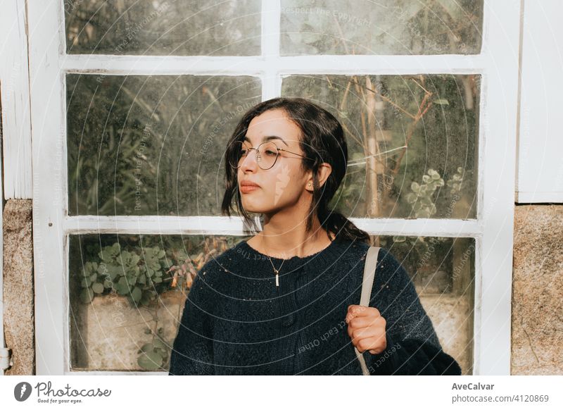 A young Moroccan woman in front of a white wooden crystal window filled with plants with copy space person lady model outside smile pretty brunette face female