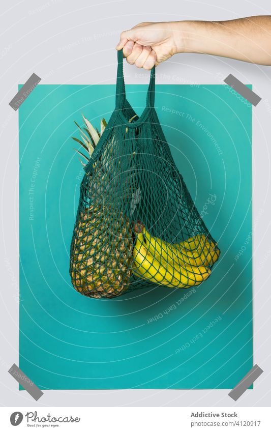 Crop person carrying string bag with pineapple adn bananas zero waste grocery concept eco friendly rectangle bright colorful organic shop blue turquoise package