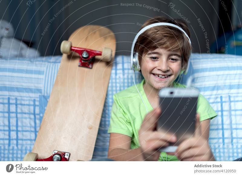 Cheerful kid with headphones using smartphone at home gadget cheerful boy laugh chat child device online listen internet happy lifestyle modern mobile