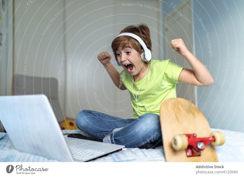 Excited boy watching match on laptop kid celebrate excited bedroom win game using home victory triumph child headphones gadget device leisure casual lifestyle