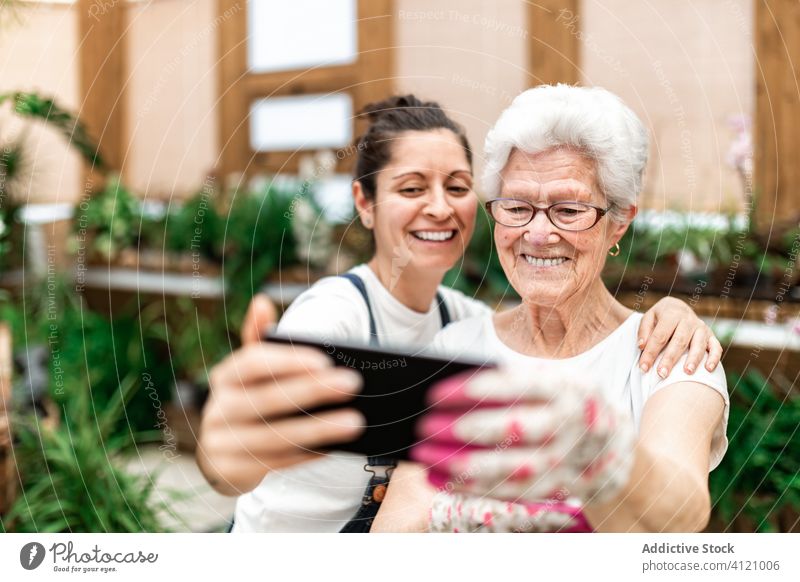 Cheerful female gardeners taking selfie women hug hothouse smartphone smile adult senior colleague work happy cheerful device gadget social media memory moment