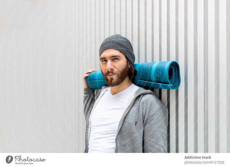Man holding yoga mat by the neck man exercise wall lean roll male casual modern training hipster cool wellness practice harmony rest relax guy lifestyle