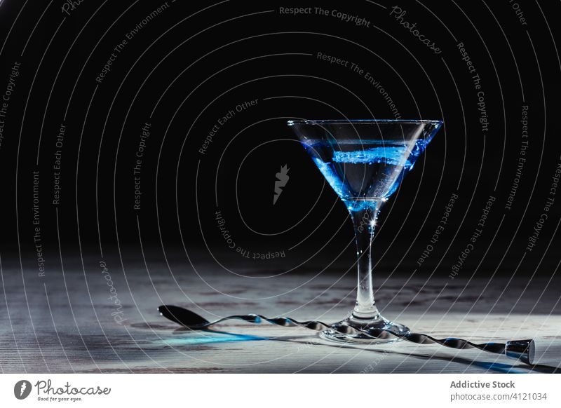 Glass of vivid blue cocktail and twisted spoon on rustic table drink alcohol ice shabby beverage dark glass long martini celebrate wooden ray colorful teaspoon