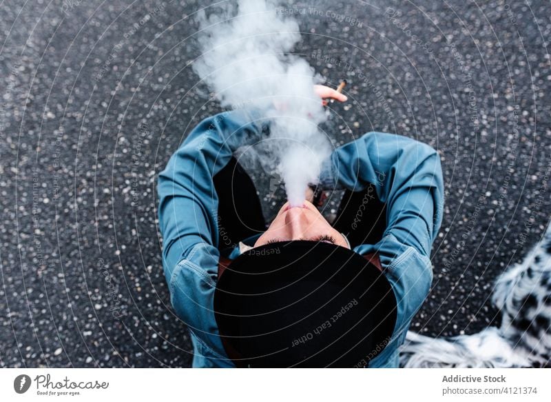 Unrecognizable woman in hat smoking cigarette on ground smoke road rest tobacco dog addict habit walk asphalt black style subculture hipster modern lounge