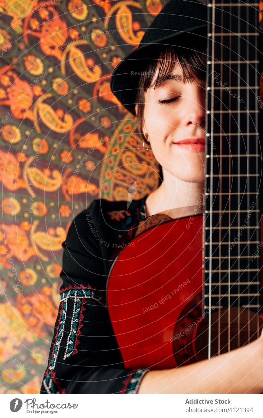 Content woman embracing guitar with eyes closed acoustic hipster hug rest home content weekend guitarist female delight serene trendy smile glad relax music