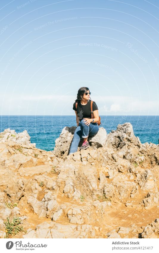 Young woman sitting on cliff near sea seashore beach harmony amazing calm sky view idyllic rock travel beautiful sunglasses nature rest freedom incredible