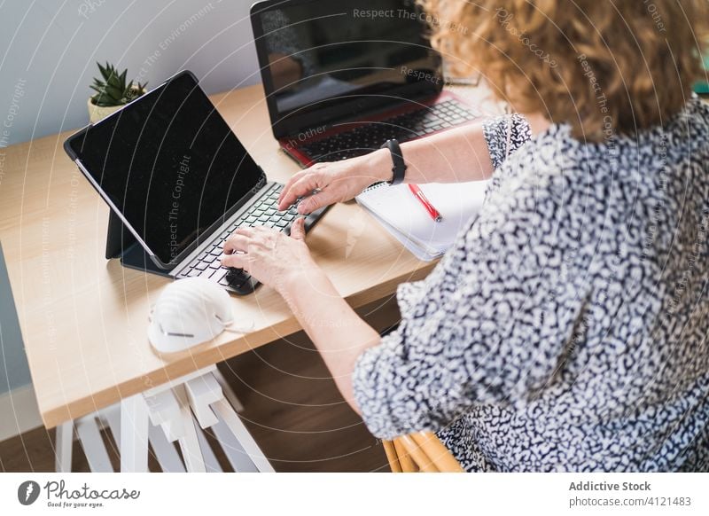 Anonymous woman working on laptops at desk at home typing keyboard table using internet browsing computer netbook business gadget device online job workplace