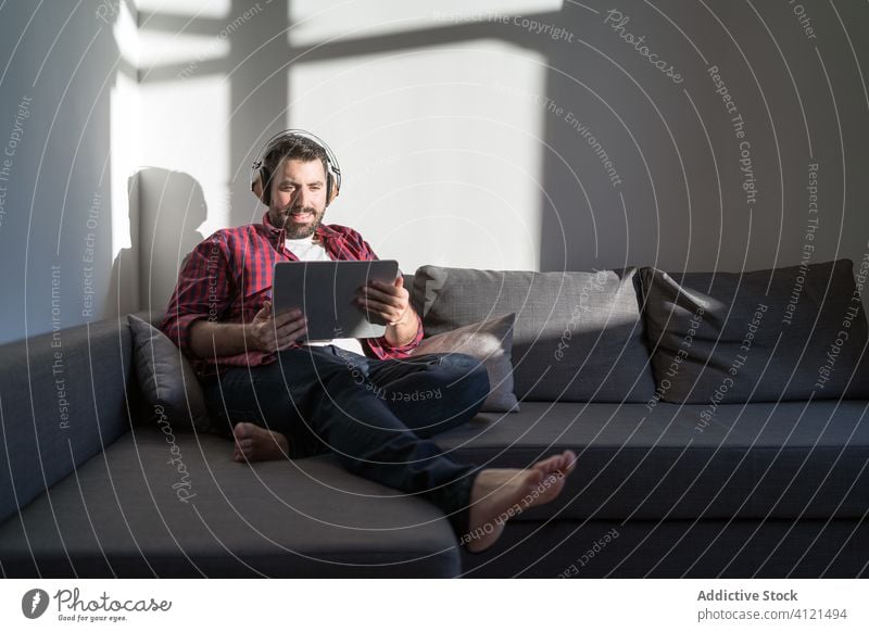 Young man listening to music at home young leisure casual headphones technology caucasian adult lifestyle happy sofa person relaxation modern room indoors
